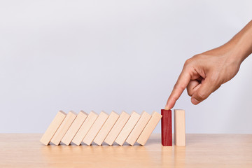 Finger stopping the domino on wooden table. Business strategy