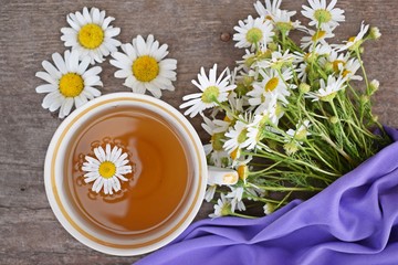 Fresh chamomile flowers and healthy tea on a lilac background.Alternative medicine.