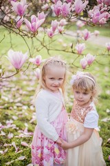 Two cute little blonde girls of 3 years old are playing in the park near a blossoming magnolia. Tea drinking. Easter.