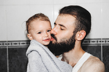 Handsome man in a white shirt holds on his hands a small daughter wrapped in a towel. Child is very...