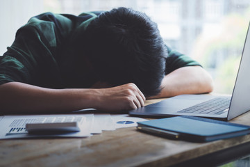 Burnout Syndrome, Man sleeping at his desk working over a laptop,Tried overworked, Freelance man working overload, Young business owner at home office,man feel tried and nap on desk.