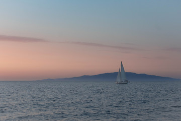 Fototapeta premium Sailboat on horizon with pink sunset
