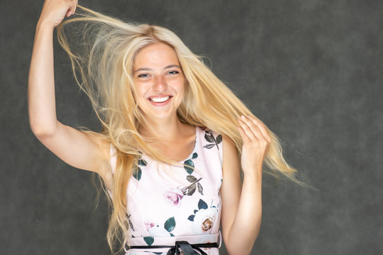 Portrait of a cute beautiful pretty woman girl with long beautiful hair on a dark gray background in a pink dress with a pattern. Shows a lot of different emotions, smiling, talking. Made in a studio.