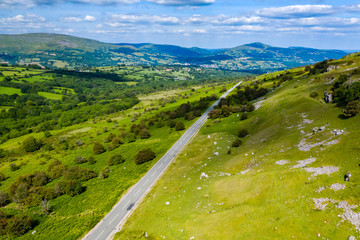 Aerial drone view of a rural road running through green farmland and rolling hills (Llangynidr,...