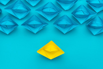 yellow paper ship stand out from the crowd over blue background. top view of race with yellow paper...