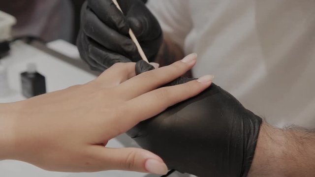 Professional manicurist man varnishes a girl's nails.