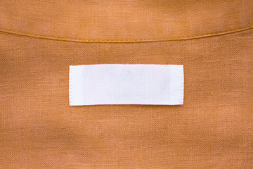 White blank clothing tag label on brown linen shirt fabric texture background