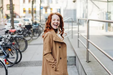 Fotobehang Frau geht durch die Stadt und schaut lachend zurück © contrastwerkstatt