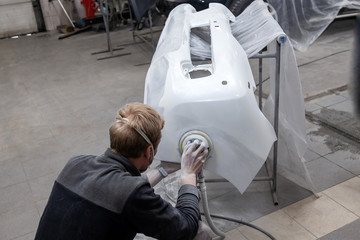 Preparation for painting a car element using sander and putty by a service technician leveling out...