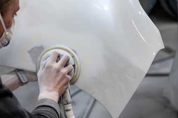 Preparation for painting a car element using sander and putty by a service technician leveling out...