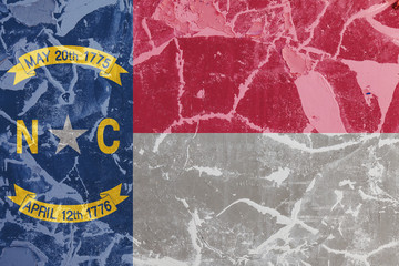The national flag of the US state North Carolina in against a gray wall with cracks and faults on the day of independence in blue red and white. Political and religious disputes, customs and delivery.