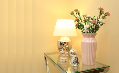 Lampka nocna i kwiaty w wazonie na szklanym stoliku i złotych barwach.