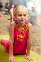 Little cute caucasian girl practicing yoga pose on mat in park. Healthy, exercise concept. Kids yoga concept. Girl is practicing yoga. Child doing exercises in the park. Healthy lifestyle.