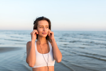 Sports fitness exercising woman on the beach listening to music