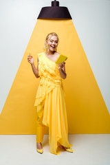 cheerful young woman looking at notebook while holding pencil on white and yellow
