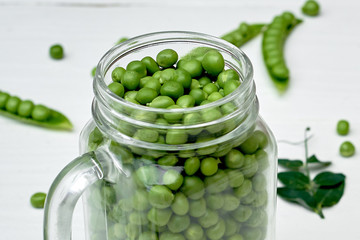Glass jar with fresh green peas on white wooden background, copy space. Bio healthy food. Pods and pea leaves on wood table