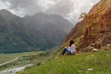 Naklejka na ściany i meble a woman with red hair in a white blouse and jeans sits against a mountain landscape, toned