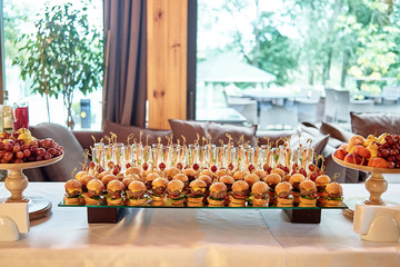 Buffet table with mini hamburgers and sliced fruits at luxury wedding reception, copy space. Serving food and appetizers at restaurant. Catering banquet table - obrazy, fototapety, plakaty