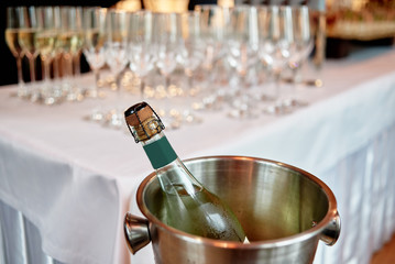 Bottle of cold wine in ice bucket with wineglasses in blur on background in restaurant, copy space. Wedding reception, holiday concept
