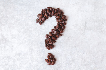 Question mark made from dark brown coffe beans on a light grey background.