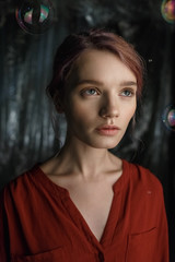 Fototapeta premium Pretty young caucasian girl in red shirt looks up. Soap bubbles fly around her head shimmering with rainbow colors.