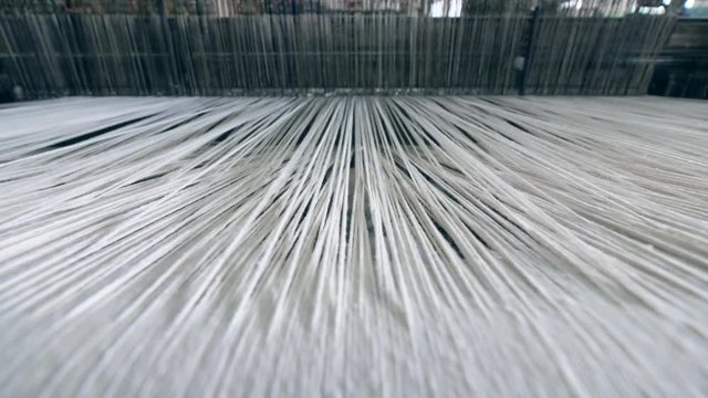 Industrial textile factory. Close up of thick white threads moving through the loom
