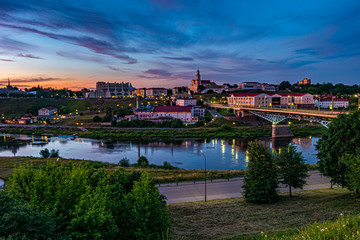 Fototapeta na wymiar panorama view on evening in old town on the bank of wide river with evening fluffy curly rolling cirrostratus clouds and blue violet red sunset sky as background