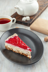 A piece of tender mascarpone cheesecake with fresh raspberry  glaze and almond flakes, served with a cup of black tea