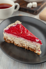 A piece of tender mascarpone cheesecake with fresh raspberry  glaze and almond flakes, served with a cup of black tea
