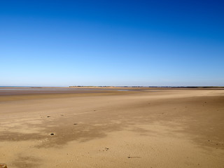 Breiter Sandstrand in der Normandie unter blauem Himmel