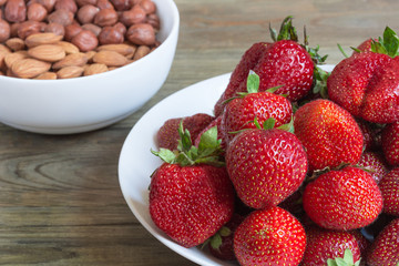 Plate of fresh strawberreis and almond, hazelnut on wooden background. Vegetarian breakfast