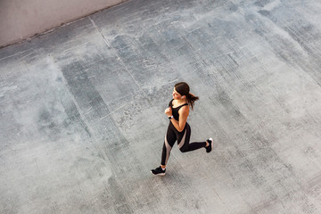 Top view of young attractive athletic woman speed running on city asphalt and workout in the morning time on a sunny summer day. Female runner training outdoor. Copyspace, sport concept