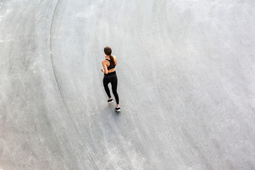 Top view of back side of young attractive athletic woman speed running on city asphalt and workout in the morning time on a sunny summer day. Female runner training outdoor. Copyspace, sport concept