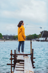 Fototapeta na wymiar woman in yellow raincoat at sea pier looking at storming water