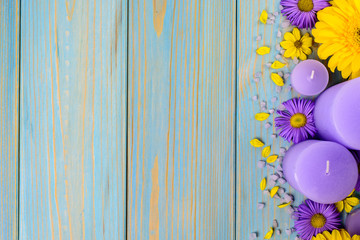 Yellow gerbera, purple garden flowers and candle on a blue wooden table. The flowers are arranged side by side. Top view, copy space.