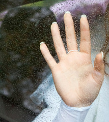 hand with a beautiful manicure on a window glass covered with raindrops