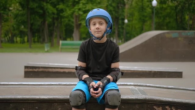 Kids sport hobby. Rollerblader in protective equipment sitting on small ramp smiling.