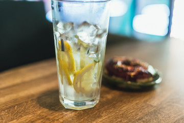 Cold lemonade with ice and lemons in a tall glass with a disposable tube. Chocolate donut with dressing.