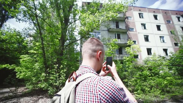 Close-up of interested young man taking photographs of abandoned buildings in overgrown green street in Prypiat city, Ukraine.