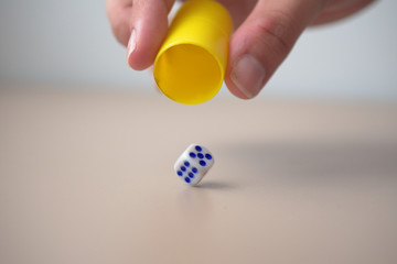 A dice is falling from the yellow beaker and it stands on the table