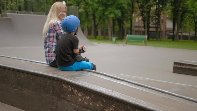 Family communication. Mother support kid rollerblading hobby. Mom and son sitting on a ramp.