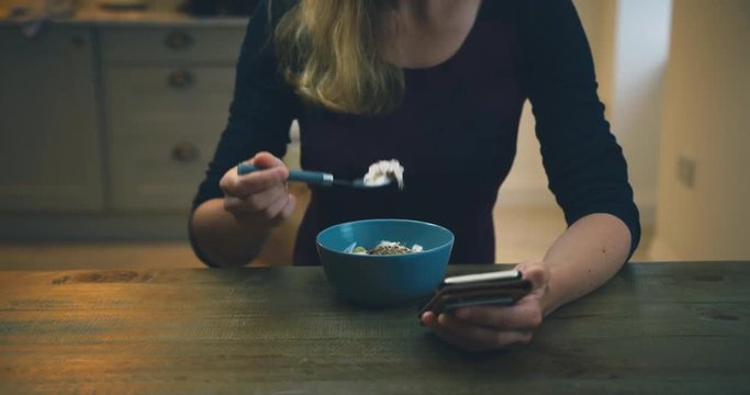 Young woman using her smartphone and having yogurt for breakfast