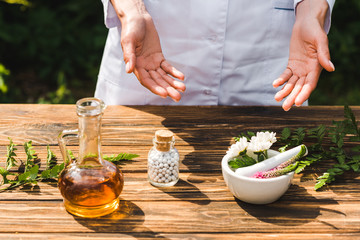 cropped view of woman near wooden table with plants and bottle with pills
