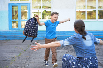 mom meets her son from elementary school. joyful child runs into the arms of his mother. a happy schoolboy runs towards his mother holding a school bag in his hands.