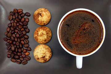 cup of black coffee with biscuits and beans on a dark plate