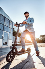 Low angle photo of smart elegant man in sunglasses and helmet which is driving his electrical scooter. © Fxquadro