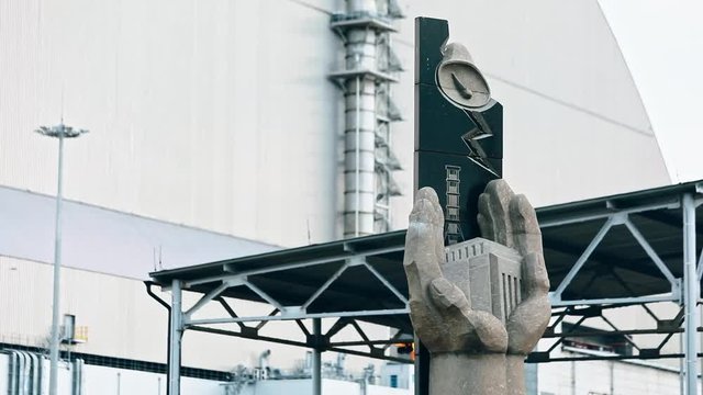 View of fantastic memorial statue against Chernobyl power plant. Well-known atomic station recent view with sarcophagus arch over fourth block reactor. Prypiat, Ukraine