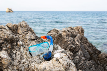 Blue snorkle or diving mask located on the rocks with sea view on the back.