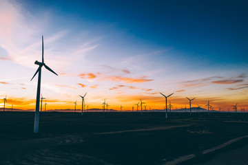Obraz premium Silhouette of windmills station with propellers generating alternative clean green power from eco resources in rural agri environment against blue sunset sky. Farm of turbines producing electricity