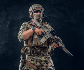 Portrait of strong manly soldier in camo uniform which is posing for photographer while holding...